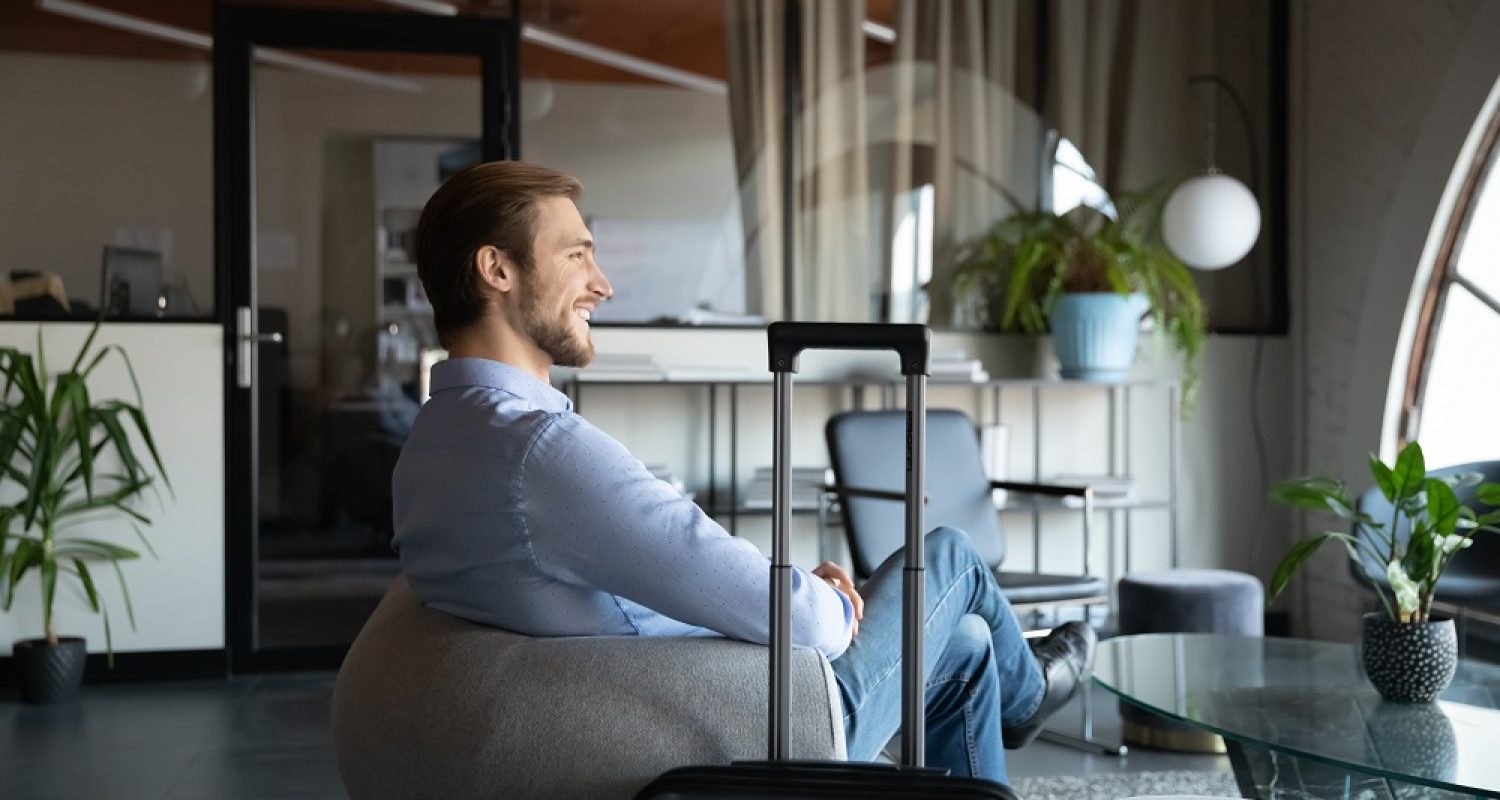 Smiling confident businessman sitting in armchair with suitcase, arrived after airport, executive waiting for meeting, appointment, entrepreneur travelling, business trip concept, foreign office